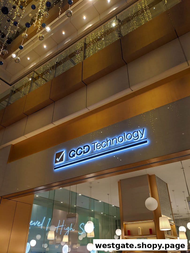 Illuminated 'QCD Technology' sign above a modern shop entrance with glass and warm lighting.