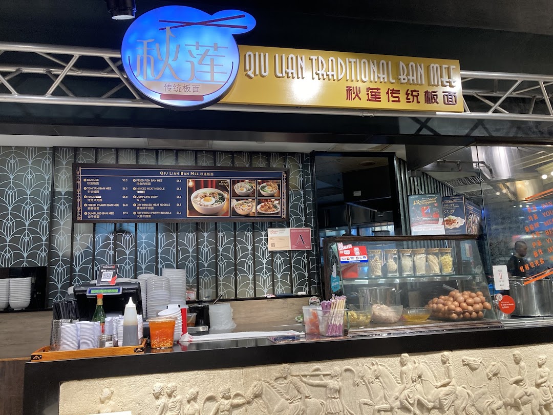 A vibrant counter view of Qiu Lian Ban Mian, featuring their menu board and fresh ingredients.