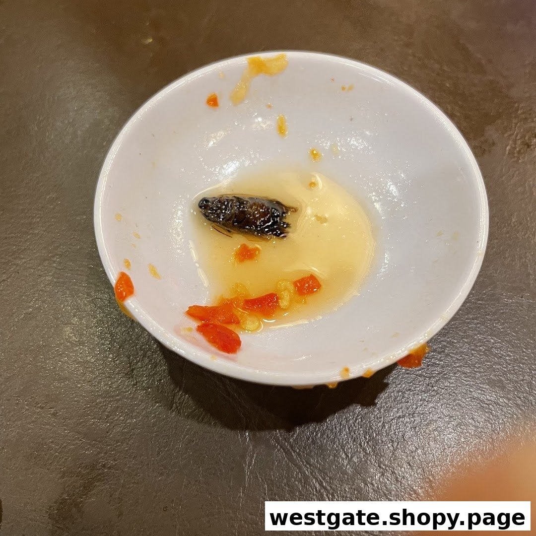 A small white bowl containing sauce, chili, and an insect on a dark table.