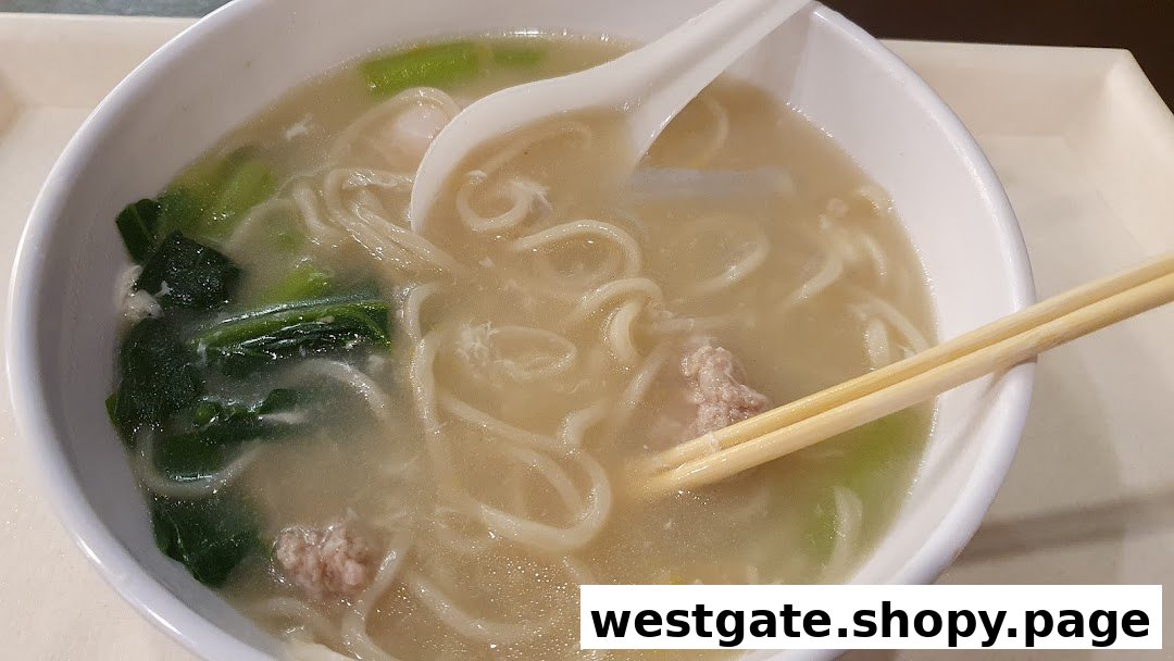 A close-up of a steaming bowl of noodles with broth, vegetables, and minced meat, served with chopsticks and a spoon.