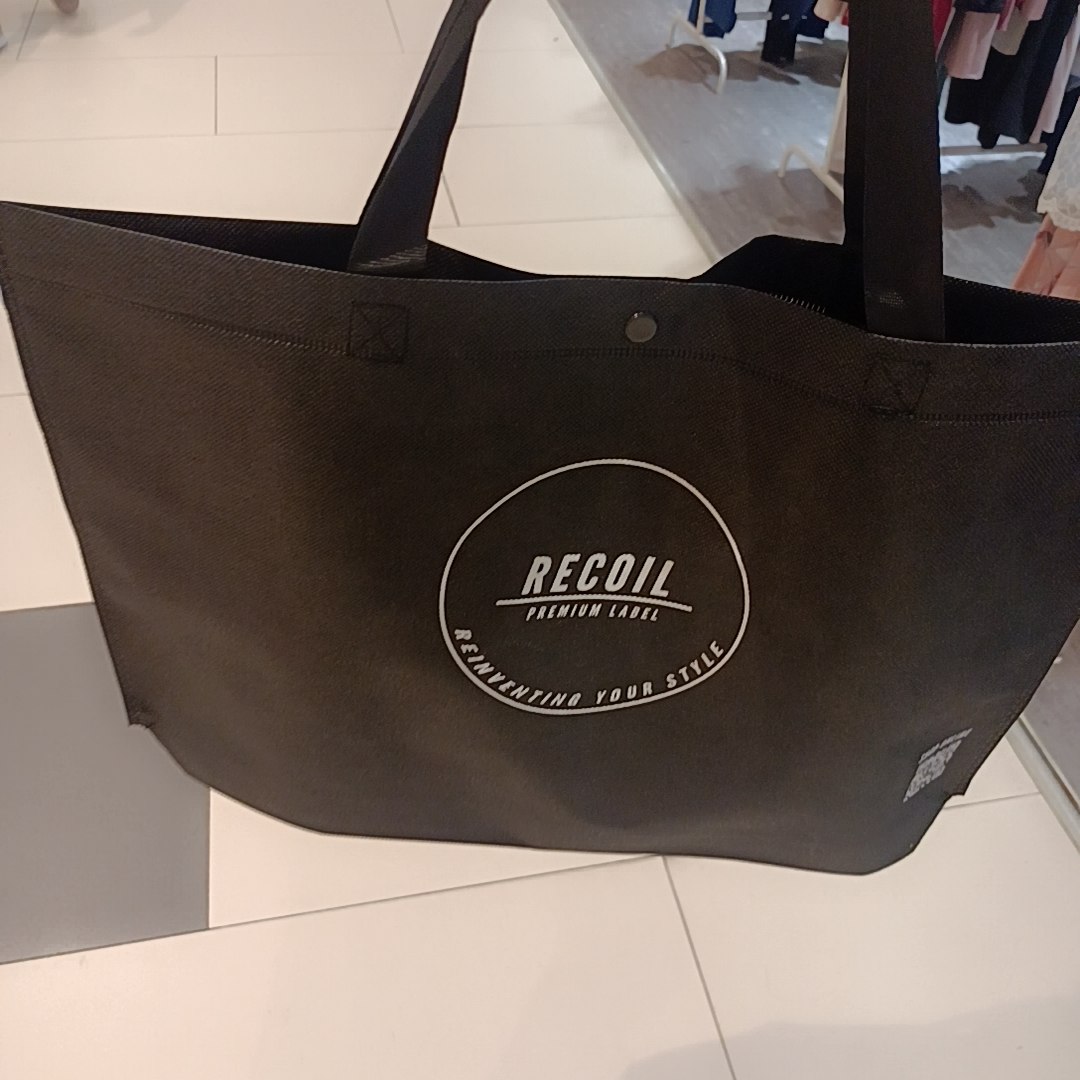 A black RECOIL shopping bag featuring the brand's logo and slogan.