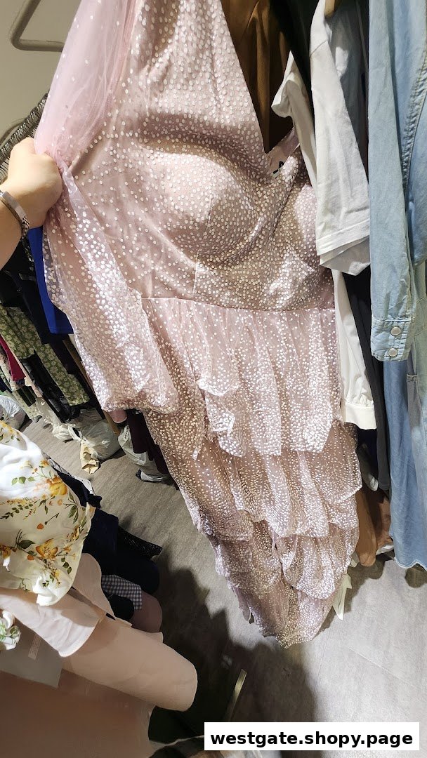A person holds up a pink, polka-dotted tiered dress from a clothing rack inside REFASH.