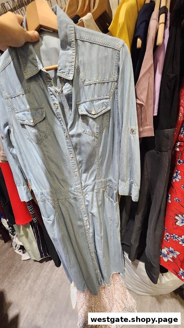 A hand holds up a light blue denim dress on a hanger inside a clothing store.
