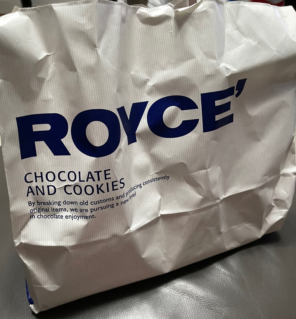 A white paper bag from Royce' featuring their brand name and a description of their chocolate and cookies.