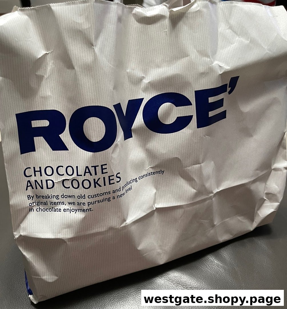 A white paper bag from Royce' featuring their brand name and a description of their chocolate and cookies.