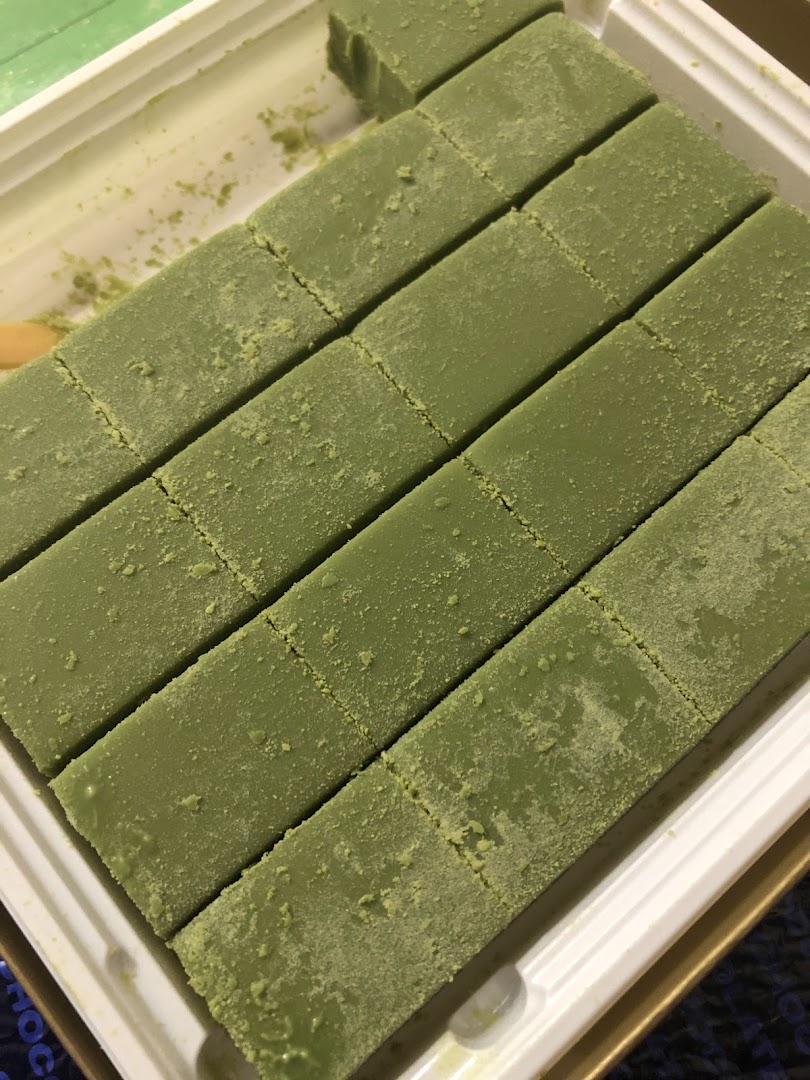 Close-up of green, matcha-dusted chocolates, likely Nama Chocolate, arranged in a white tray.