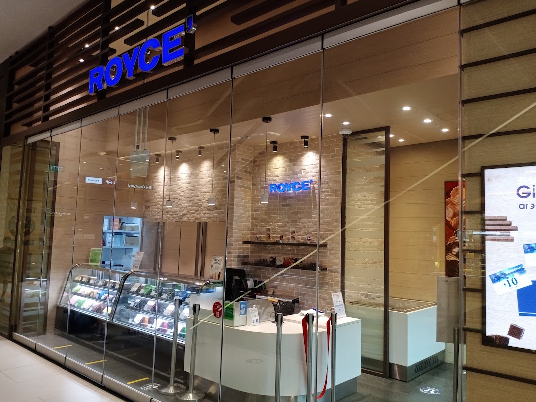 The modern storefront of Royce, a chocolate shop, featuring its blue illuminated sign and display cases.