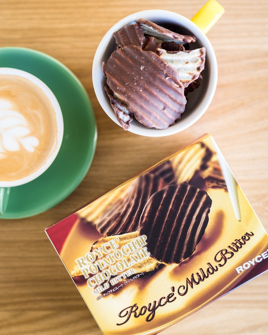 Overhead view of Royce's chocolate potato chips, a box, and a coffee cup on a wooden table.