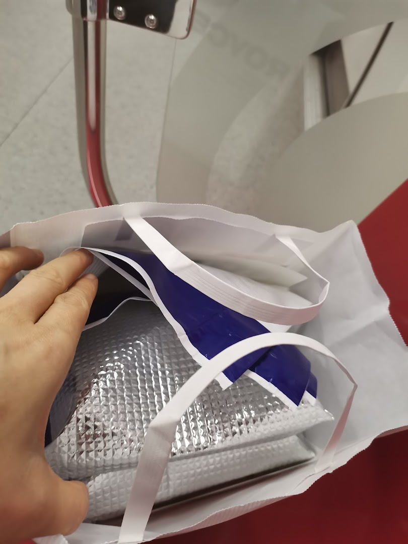A hand holds a white shopping bag containing an insulated silver bag from Royce.