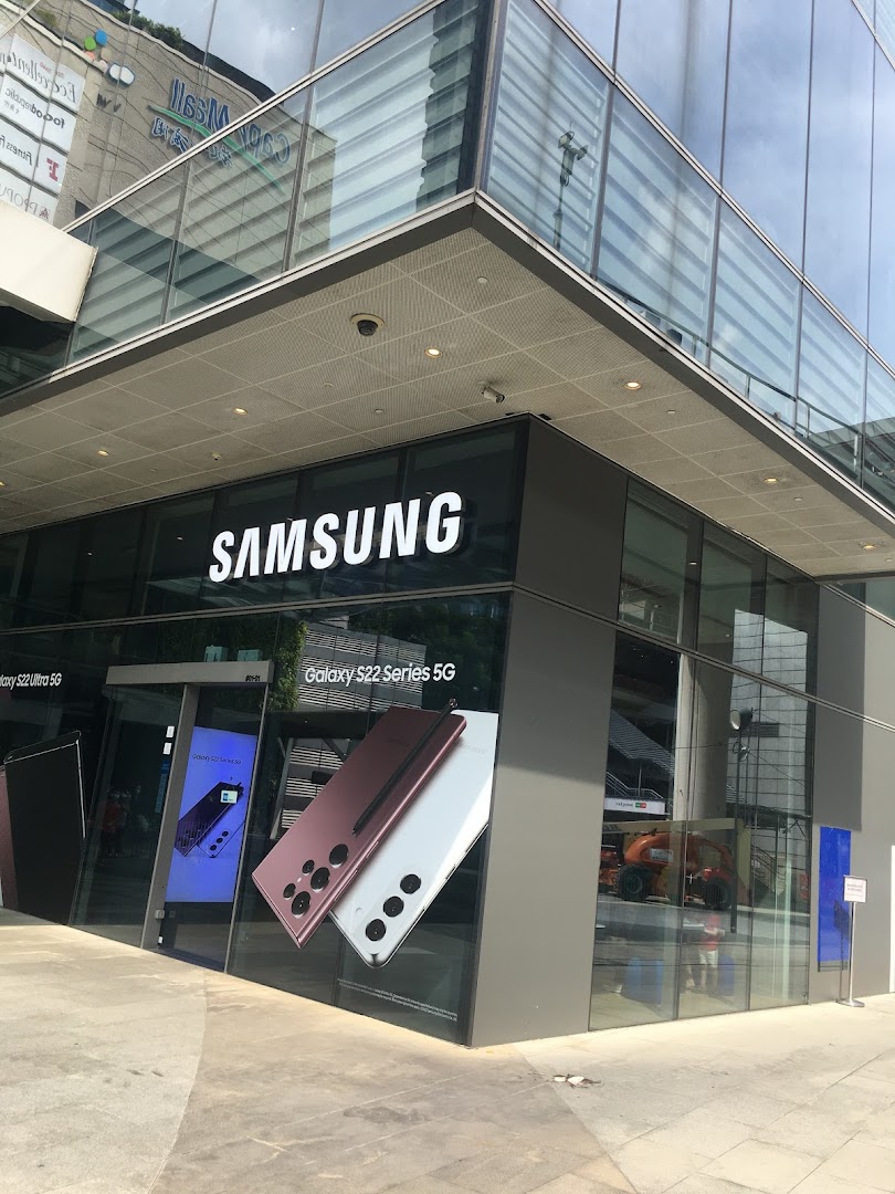 The modern exterior of a Samsung Experience Store featuring large glass windows and displays of the latest Galaxy S22 Series 5G phones.