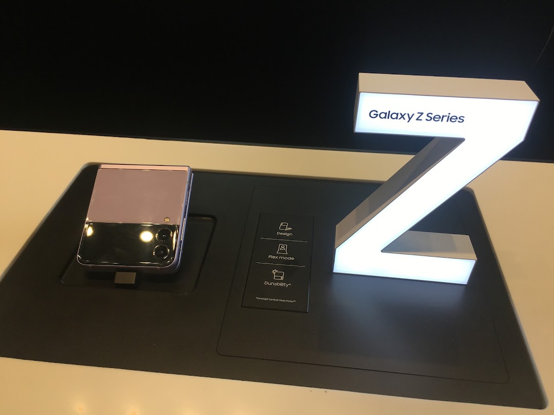 A Samsung Galaxy Z Flip phone displayed on a stand next to a lighted 'Galaxy Z Series' sign.