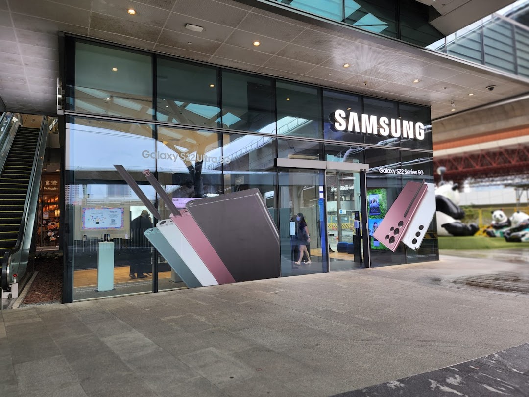 Exterior view of the Samsung Experience Store, showcasing large glass windows with promotional graphics for Galaxy S22 series phones.