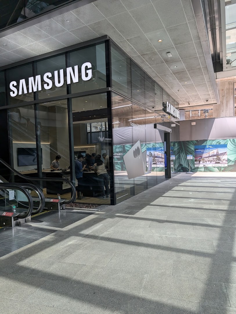 The modern glass facade of a Samsung Experience Store, showcasing its entrance and interior with customers.