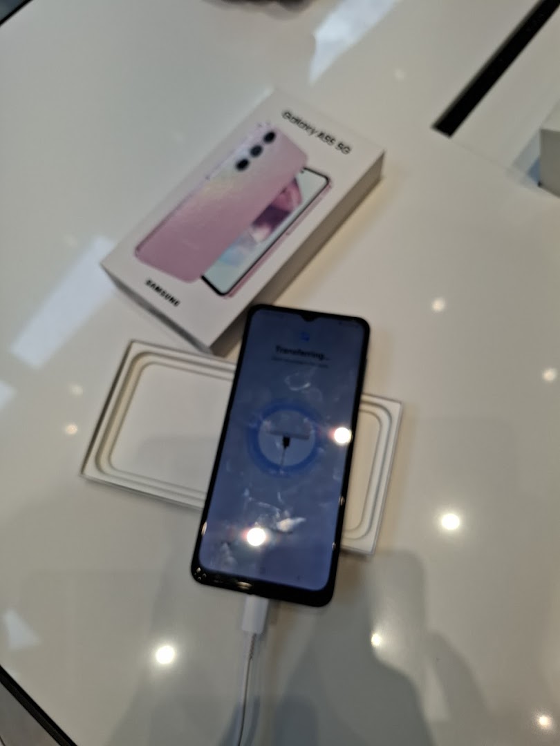 A Samsung Galaxy A55 5G phone is shown charging next to its open box on a white display.