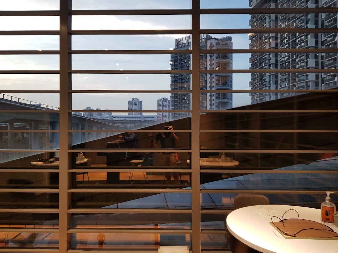 An interior view of the Samsung Service Centre, looking out through window blinds at a city skyline and reflections of the waiting area.