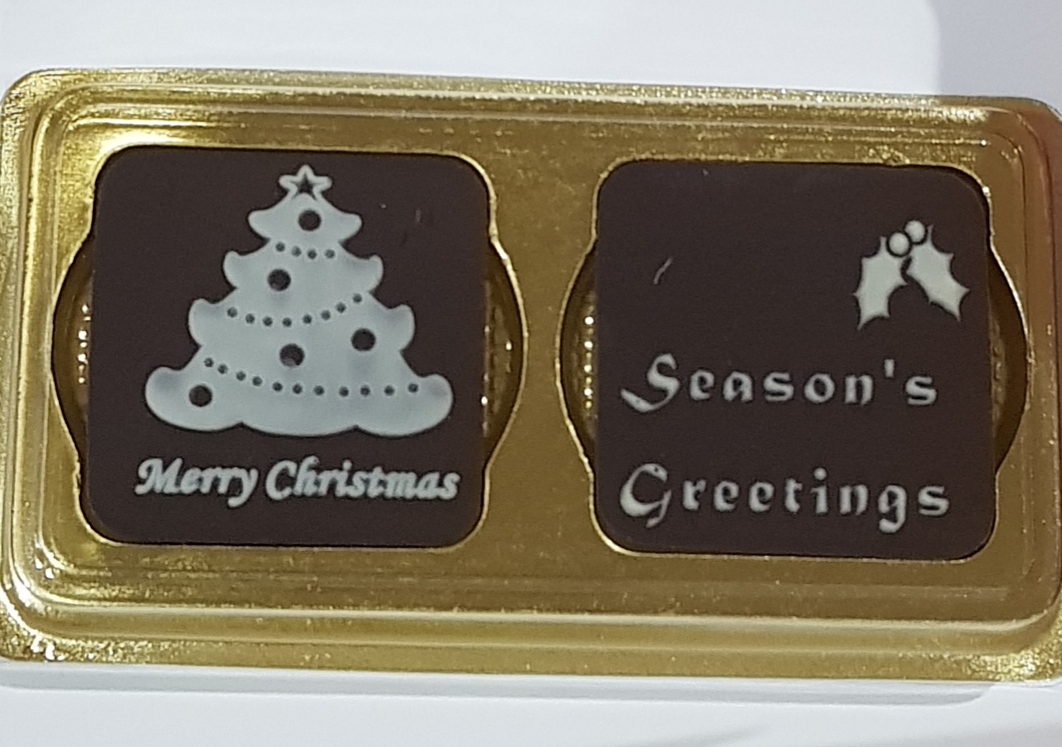 Two festive chocolates in a gold tray, one with a Christmas tree, the other with 'Season's Greetings'.