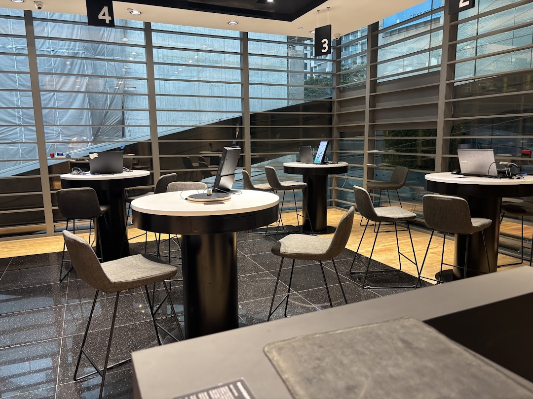 Interior view of a modern Samsung Service Centre with high-top tables, chairs, and laptops.
