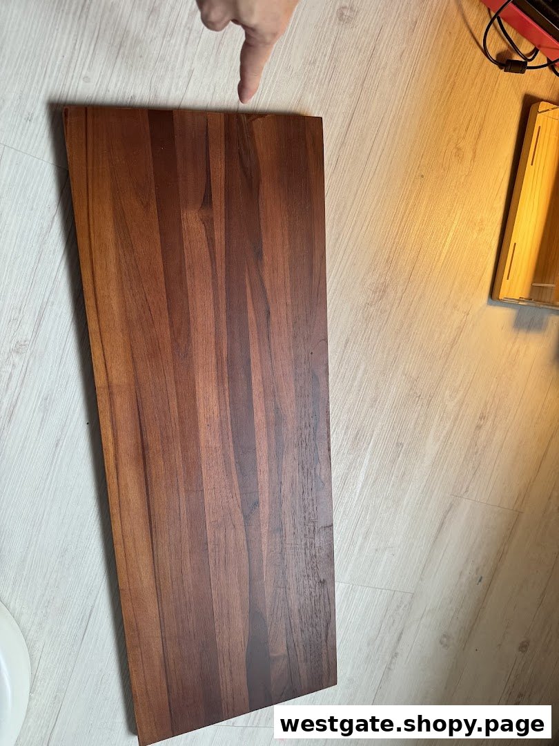 A hand points to a rich teak wood plank on a light floor, showcasing its natural grain.
