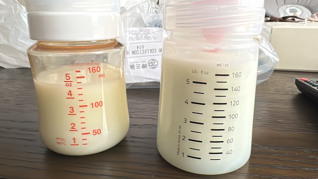 Two baby bottles, one with red markings and one with black, filled with milk on a wooden surface.