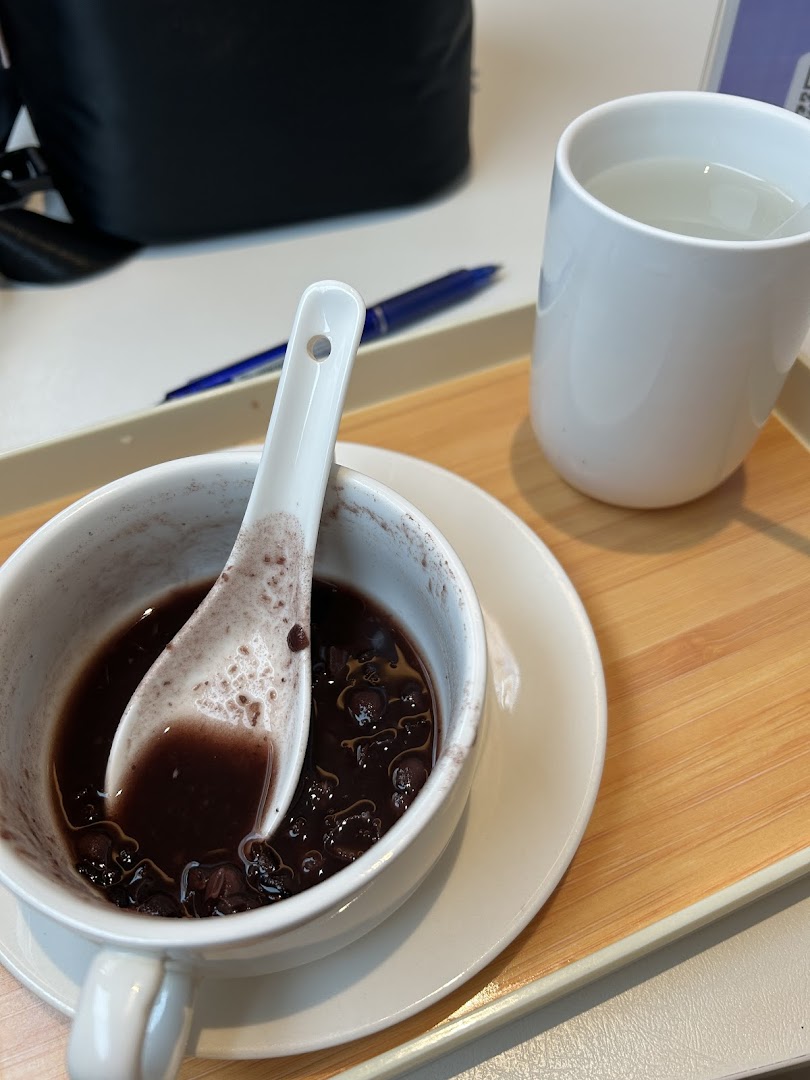 A close-up of a delicious black bean dessert with a spoon and a cup of water on a tray.
