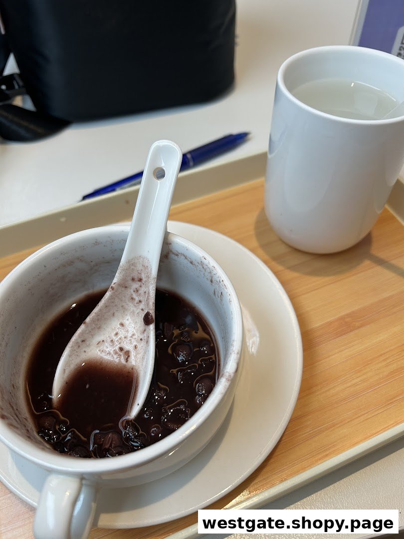A close-up of a delicious black bean dessert with a spoon and a cup of water on a tray.