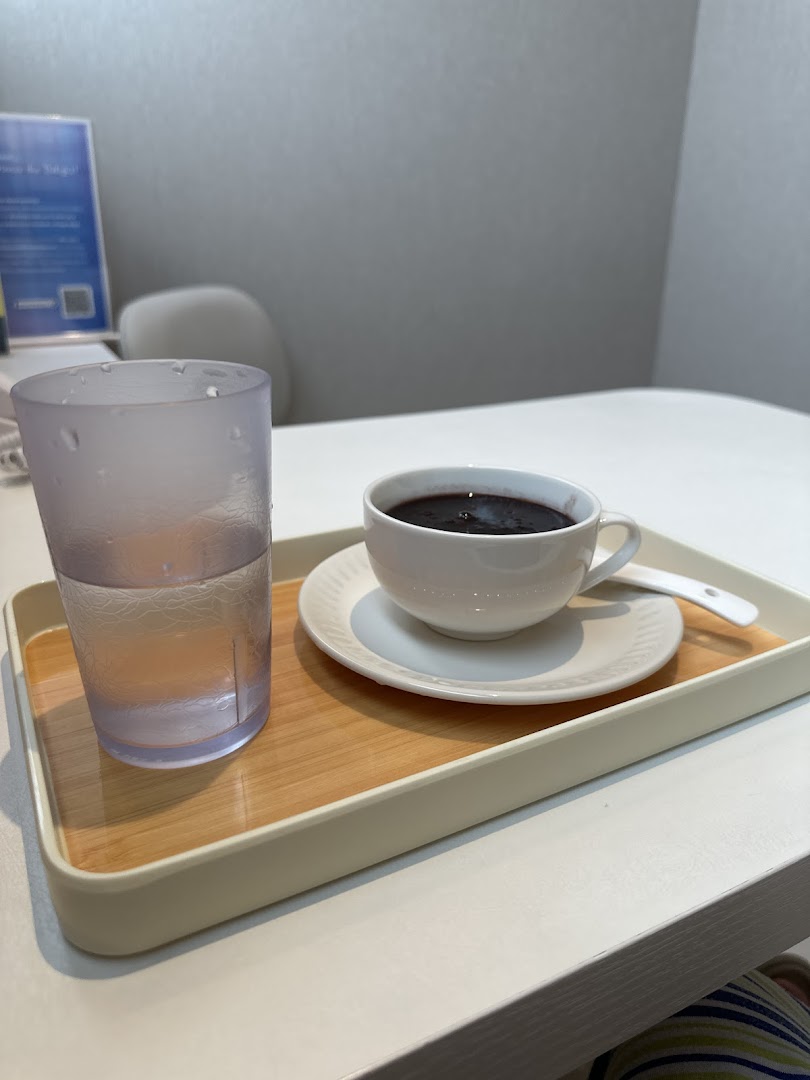 A cup of dark beverage and a glass of water on a tray, served on a white table.