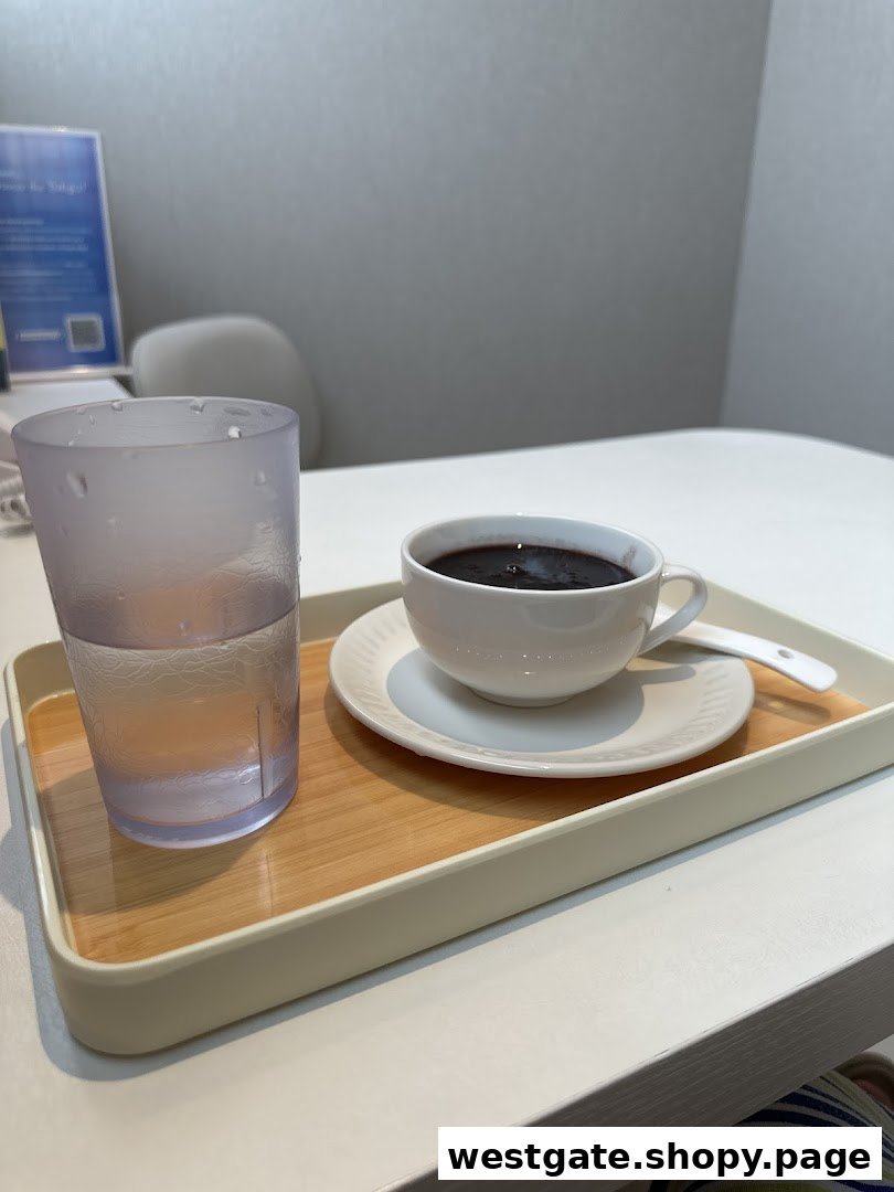 A cup of dark beverage and a glass of water on a tray, served on a white table.