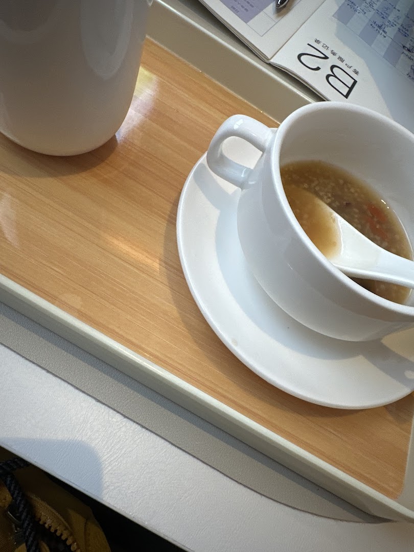 A close-up of a comforting meal on a tray, featuring a bowl of soup or congee and a cup.