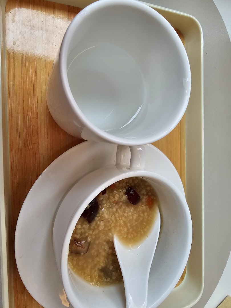 A bowl of wholesome porridge with a spoon and an empty cup, served on a wooden tray.