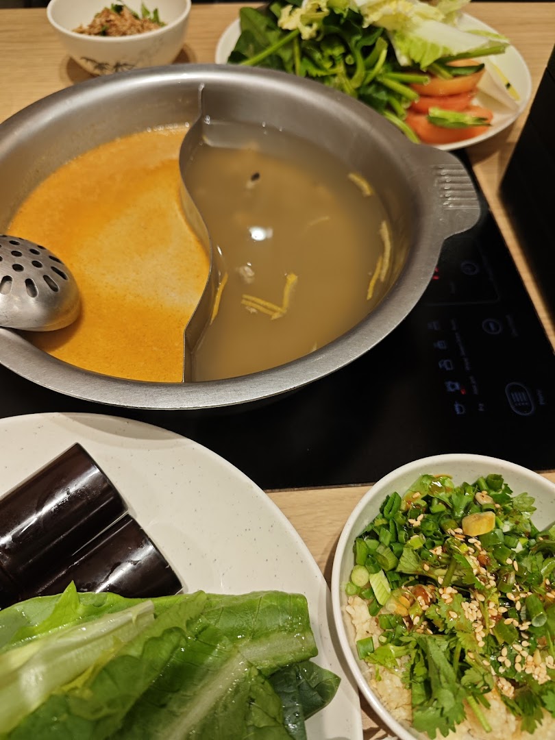 A hot pot with two broths, fresh vegetables, and condiments ready for a delicious meal.