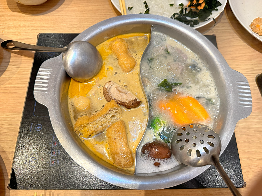 A bubbling hot pot with two distinct broths and various ingredients cooking on a tabletop induction cooker.