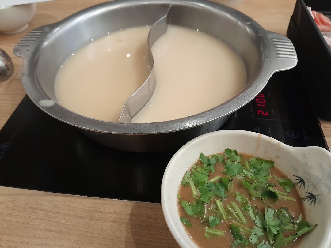A hot pot with two distinct broths and a side of dipping sauce, ready for a meal.