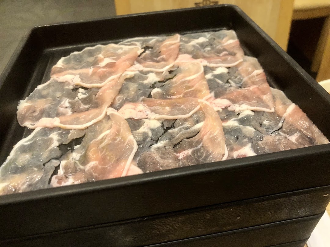 A black tray filled with thinly sliced raw meat, likely pork or beef, ready for shabu-shabu.