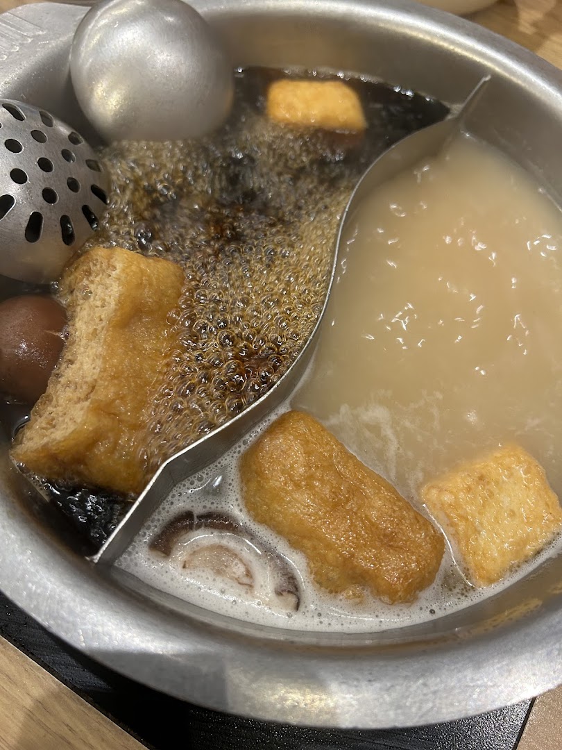 A close-up of a bubbling hot pot with two distinct broths and various ingredients.