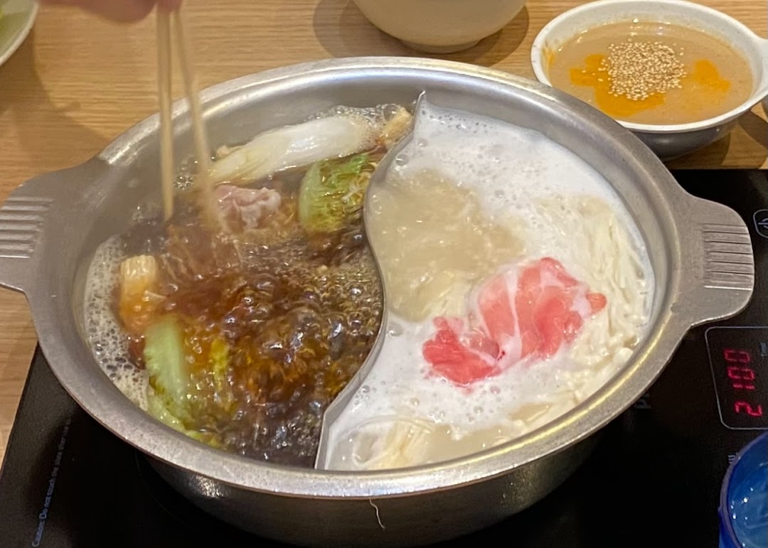 A bubbling hot pot with two distinct broths, meat, and vegetables, ready to be enjoyed.