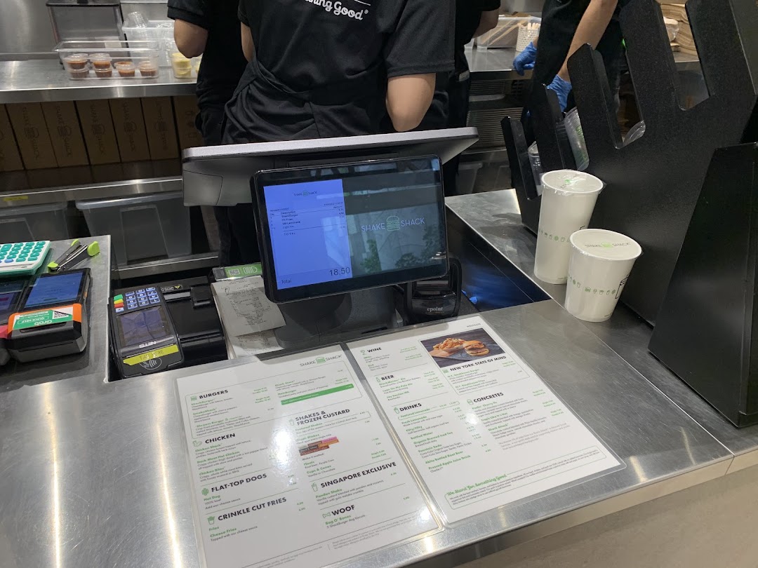 A close-up of the Shake Shack counter with a digital display, payment terminal, and physical menu.