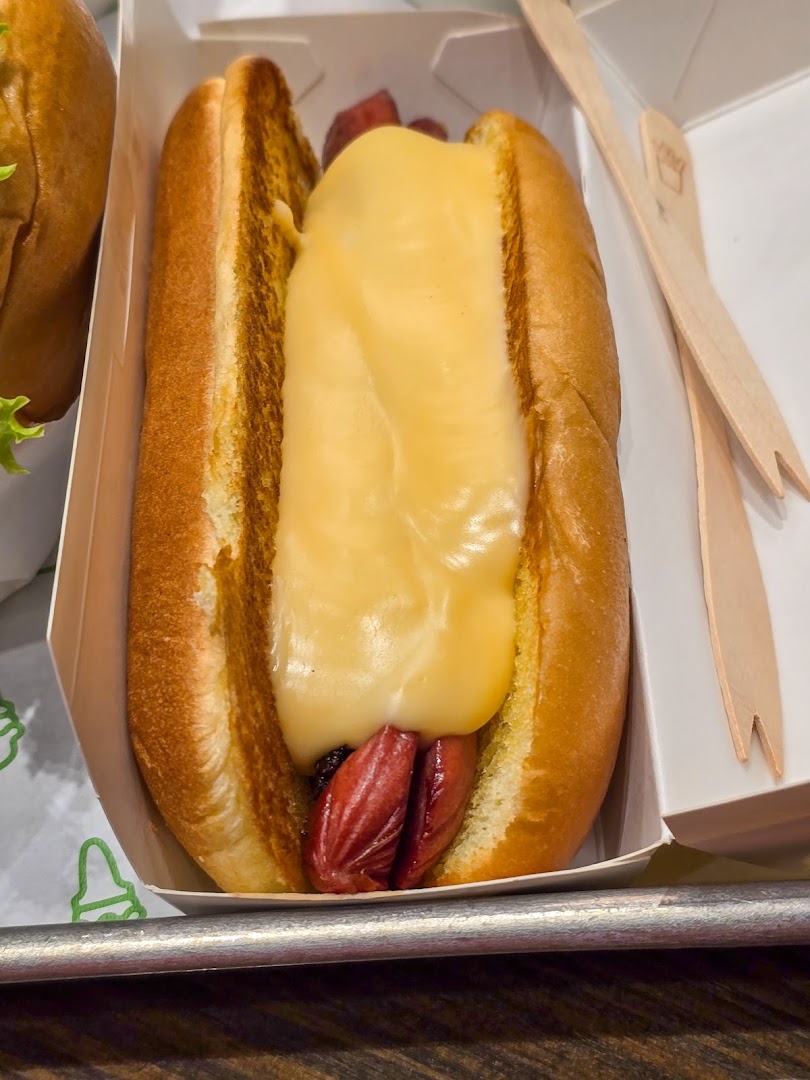 A delicious hot dog topped with melted cheese sauce in a Shake Shack box.