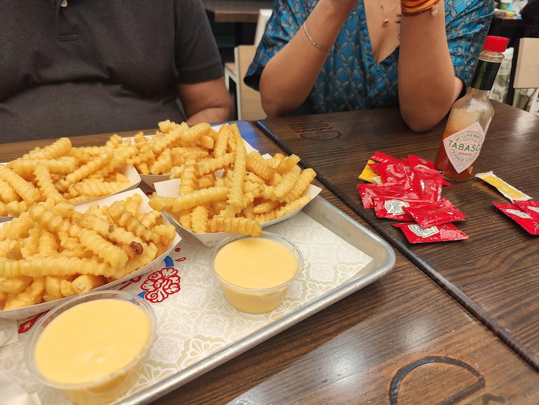 Close-up of Shake Shack's signature crinkle-cut fries with cheese sauce and condiments on a wooden table.