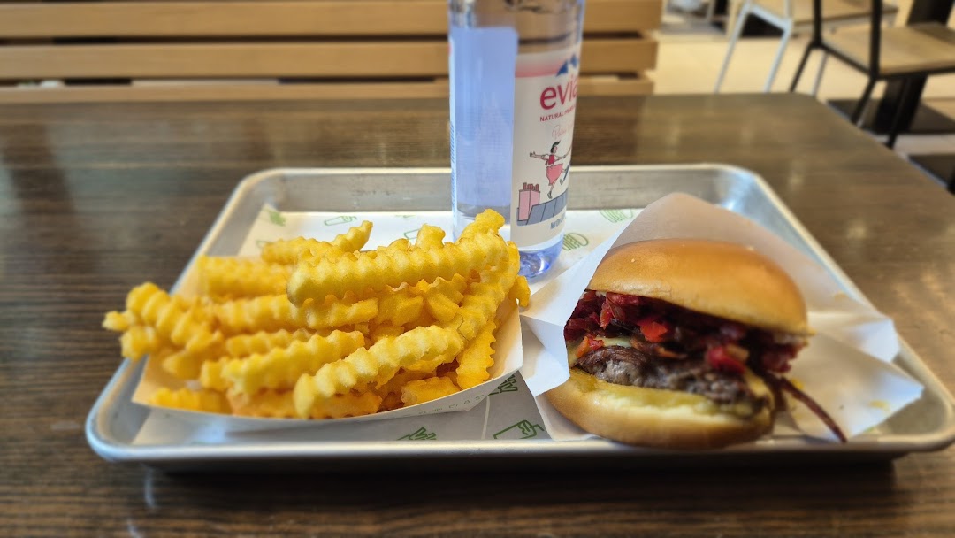 A tray featuring a Shake Shack burger, crinkle-cut fries, and an Evian water bottle.
