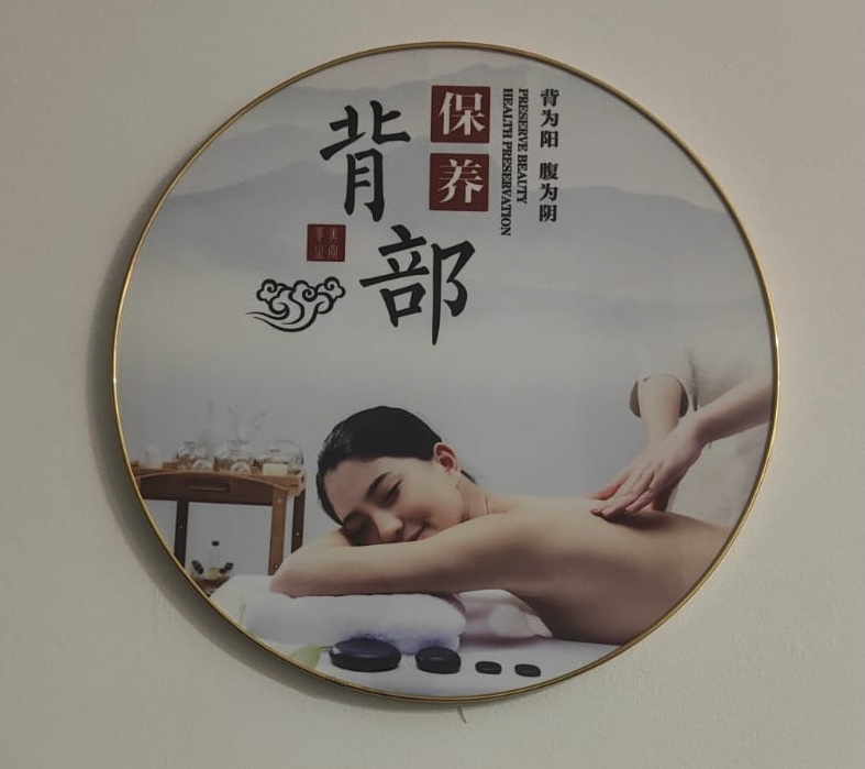 A circular wall art piece featuring a woman receiving a back massage, with traditional Chinese wellness text.