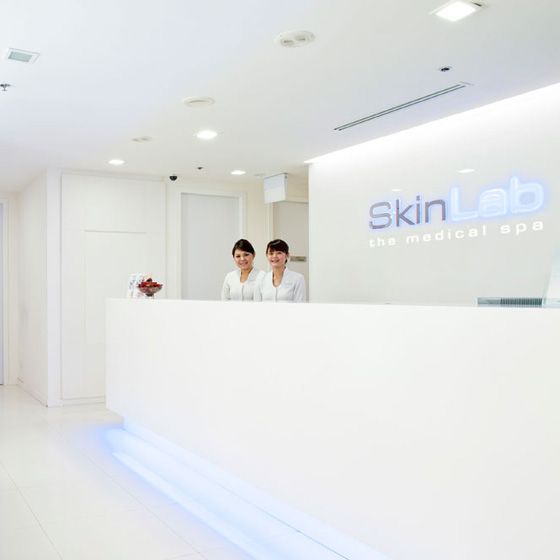 Two friendly staff members stand behind a sleek white reception desk at SkinLab The Medical Spa.