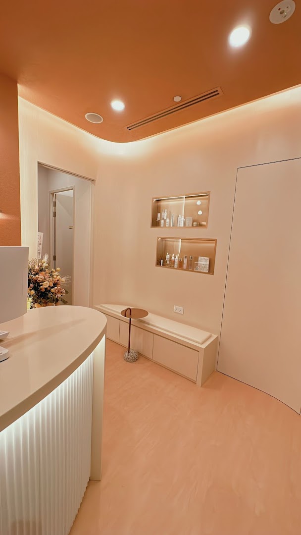 A modern, peach-toned aesthetic clinic interior featuring a reception desk, waiting bench, and product displays.