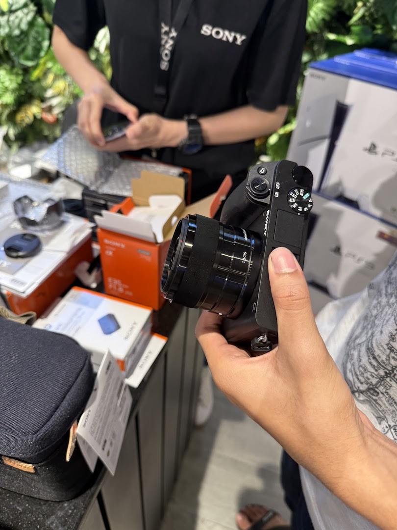 A customer holds a Sony camera while a staff member assists at the counter, surrounded by Sony products.
