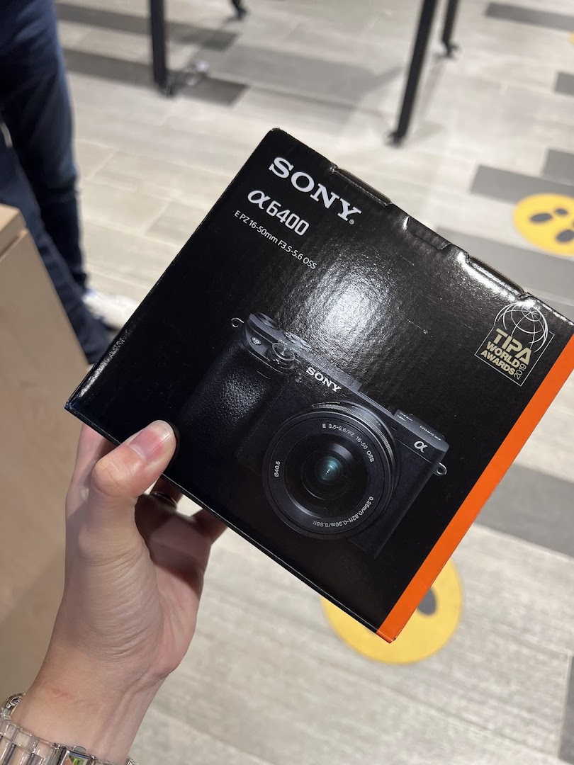 A hand holds a Sony Alpha 6400 camera box, showcasing the product in-store.