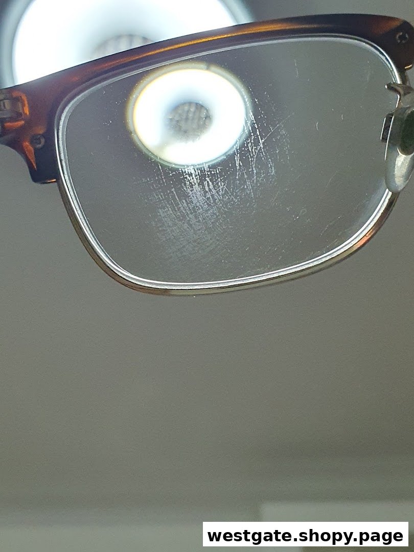 A close-up of an eyeglasses lens with visible scratches and a bright light reflection.