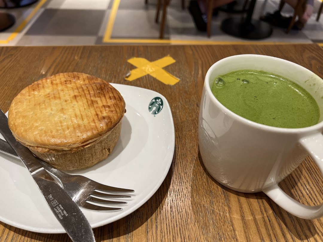 A golden-brown pie and a green matcha latte on a wooden table at Starbucks.