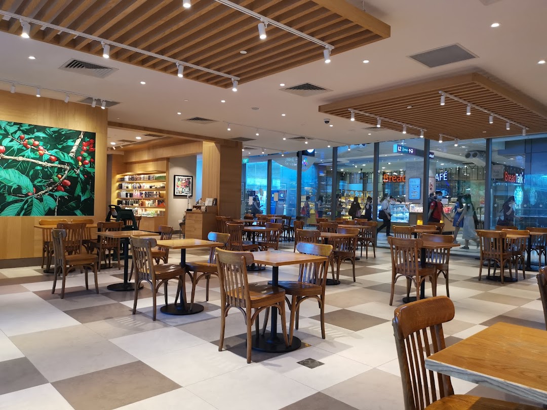 Spacious interior of Starbucks Westgate with wooden tables, chairs, and a large coffee plant mural.