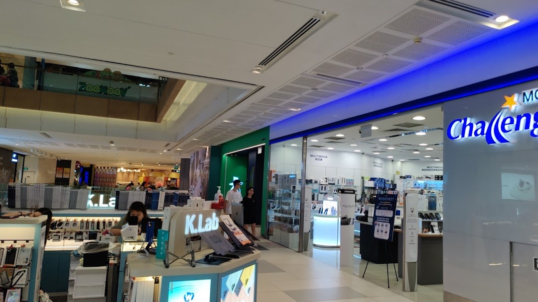 A bustling shopping mall interior featuring electronics stores and shoppers.
