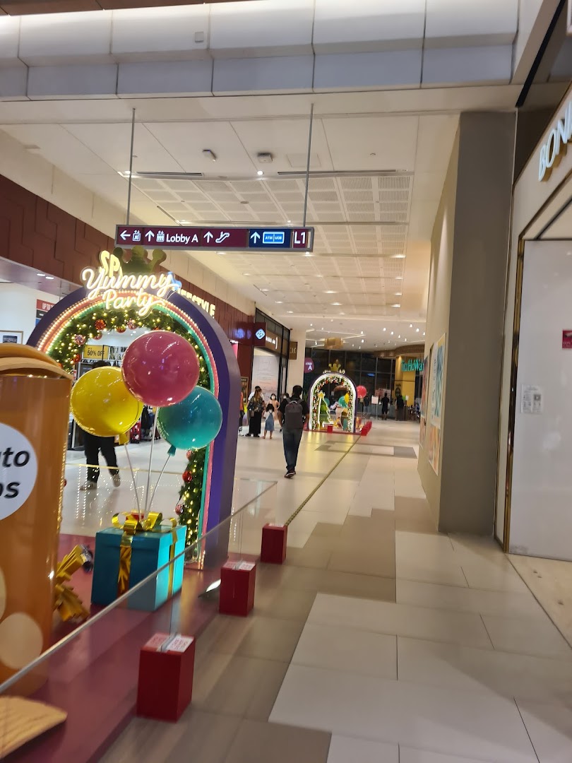 A bustling mall corridor adorned with festive 'SP Yummy Party' decorations, featuring balloons and gift boxes.