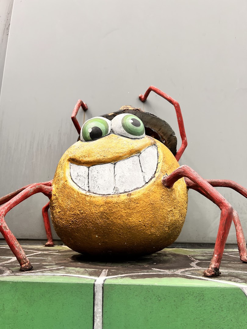 A large, smiling, cartoonish insect sculpture with big eyes and red legs.